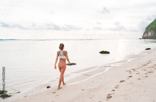 Woman in sportswear walking along sandy seashore