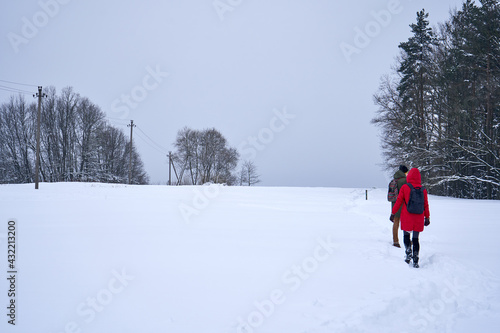 People walking in the snow in the field near the forest. 