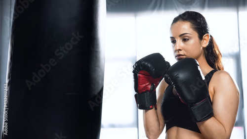 sportswoman in boxing gloves and sportswear exercising with punching bag in gym. © LIGHTFIELD STUDIOS