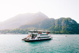 Peaceful Lake Como (Italian Lago di Como). Big ferry boat transportation with cars and people in amazing harbor. Small coastal resort town in Alps. Scenic panorama. Nautical vessel. Forest and hills.