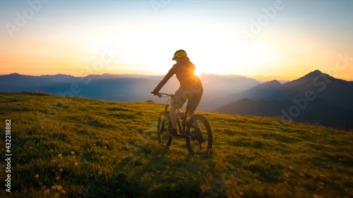 Fototapeta Naklejka Na Ścianę i Meble -  Woman riding mountain bike into the sunset. Beautiful golden summer light.