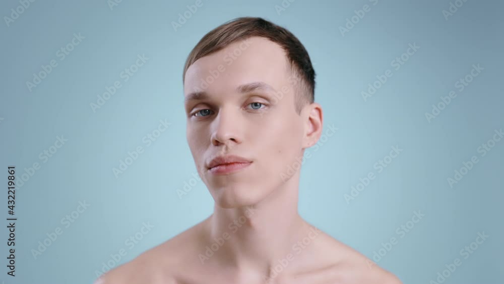 Headshot of millennial man touching his face while looking to camera . Portrait of male handsome model with naked shoulders and blue eyes posing . Concept of cosmetology and skincare. Headshot of millennial man touching his face while looking to camera . Portrait of male handsome model with naked shoulders and blue eyes posing . Concept of cosmetology and skincare.
