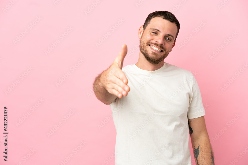Young Brazilian man isolated on pink background shaking hands for closing a good deal Young Brazilian man isolated on pink background shaking hands for closing a good deal