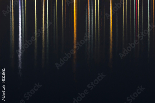Colorful seaside evening lights reflection, vertical lines on dark background; color photo.