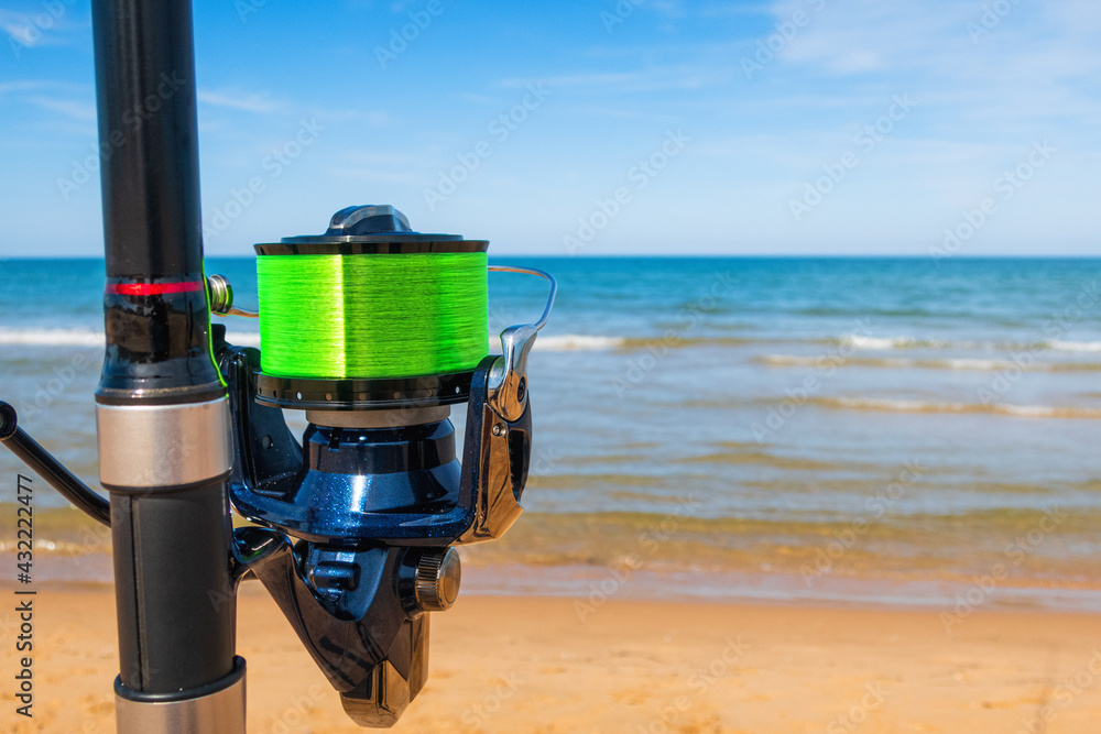 Close-up spinning reel of a fishing rod, with the sea in the background. Close-up spinning reel of a fishing rod, with the sea in the background.