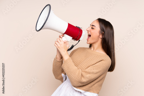 Young caucasian woman isolated on beige background shouting through a megaphone