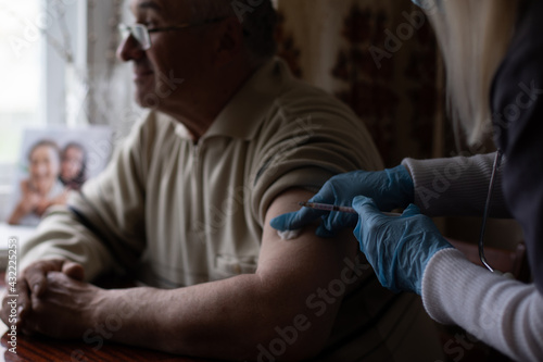 Doctor preparing vaccination shot to elderly patient by holding syringe at home - concept of home health check to seniors during coronavirus covid-19 pandemic