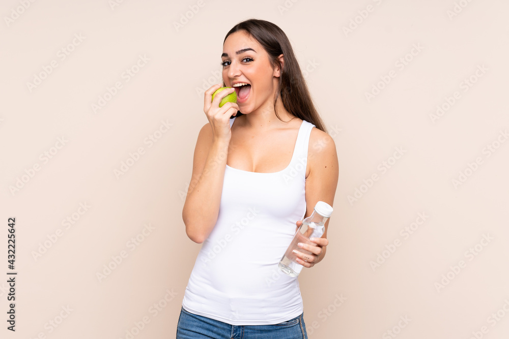 Young caucasian woman isolated on beige background with a bottle of water and eating an apple Young caucasian woman isolated on beige background with a bottle of water and eating an apple