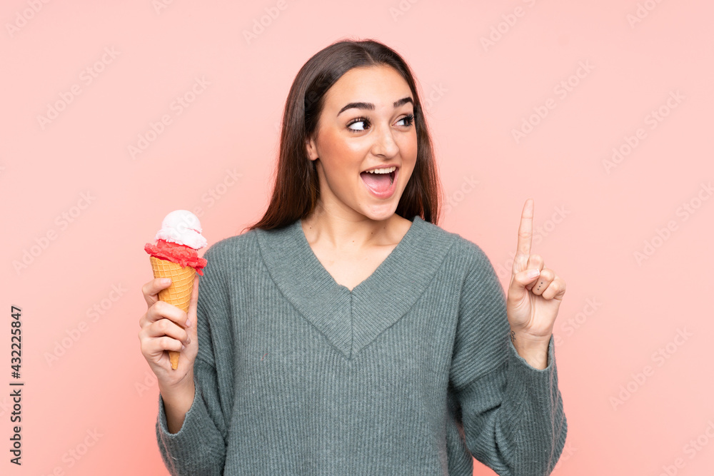 Young woman holding a cornet ice cream isolated on pink background intending to realizes the solution while lifting a finger up Young woman holding a cornet ice cream isolated on pink background intending to realizes the solution while lifting a finger up