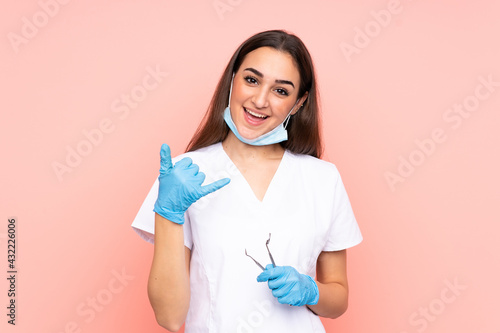 Woman dentist holding tools isolated on pink background making phone gesture