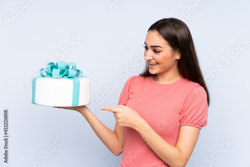 Pastry chef holding a big cake isolated on blue background pointing to the side to present a product © luismolinero