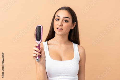 Young caucasian woman isolated on beige background with hair comb