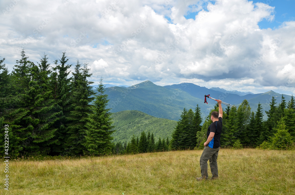 Man on the mountain meadow raised his hand with trekking poles enjoying at the beautiful mountain view. Carpathians, Ukraine