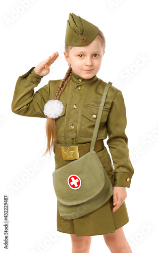 A little girl with a long pigtail and a white bow in a Soviet military nurse's uniform salutes on a white background. Concept for the Victory Day in World War II on May 9
