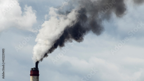 Industrial smoke from chimney on dramatic sky background. View of high chimney pipes with grey smoke from coal power plant. Production of electricity with fossil fuel. Wind blowing pollution.