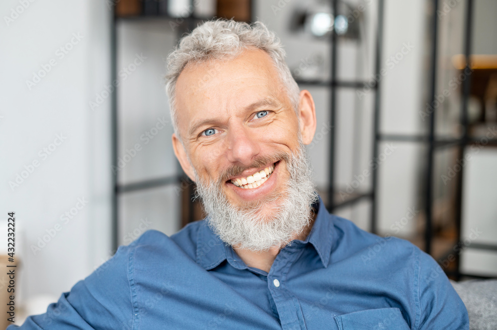 Headshot of handsome charismatic mature man in casual shirt. Close Up portrait of bearded grey-haired middle-aged male, he looks at the camera with a cheerful toothy smile Headshot of handsome charismatic mature man in casual shirt. Close Up portrait of bearded grey-haired middle-aged male, he looks at the camera with a cheerful toothy smile