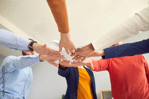 Team of happy business people put hands together. Group of teammates standing in circle join hands showing unity and motivation to reach success. Crop low angle shot, view from below. Teamwork concept