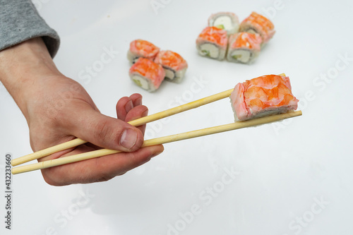 hand holding sushi sticks, against the background of a large portion of rice dishes of Asian cuisine, food with traditional tools