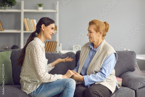 Fototapeta Naklejka Na Ścianę i Meble -  Grown-up daughter talking to senior mother. Happy daughter and friendly mother-in-law sitting on sofa and having sincere honest conversation. Mutual understanding, family supporting each other concept