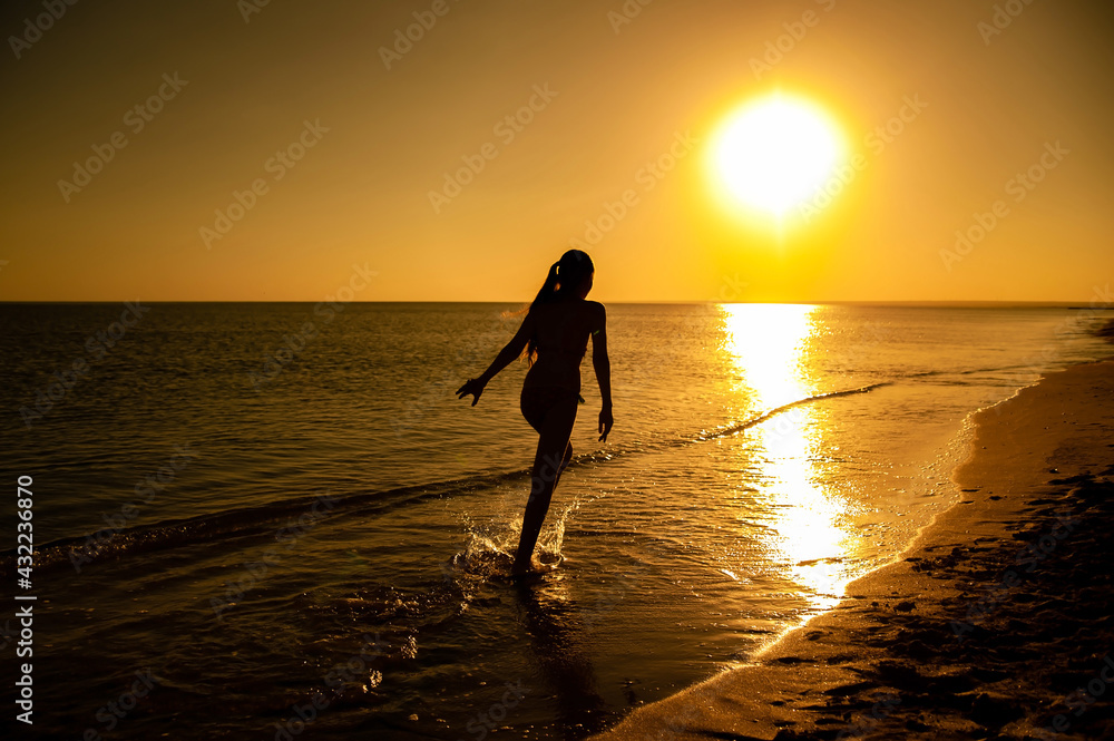 Silhouette of a girl running along the edge of the water in the sea at sunset. Recreation and sports concept