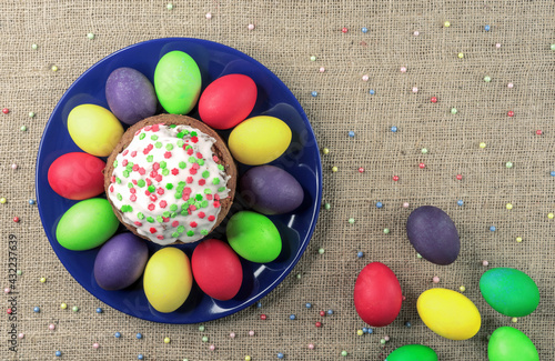 Round plate with multicolored Easter eggs and Easter cake on a burlap background. photo