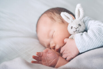 Newborn sleep at first days of life. Portrait of new born baby one week old with cute soft toy in crib in cloth background.