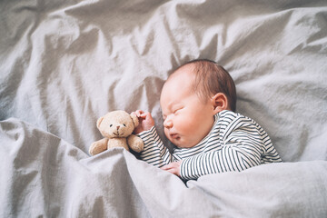 Newborn sleep at first days of life. Portrait of new born baby one week old with cute soft toy in crib in cloth background.