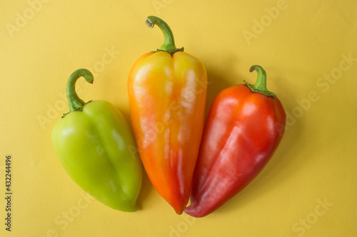 green, orange and red bell peppers isolated on yellow background . High quality photo