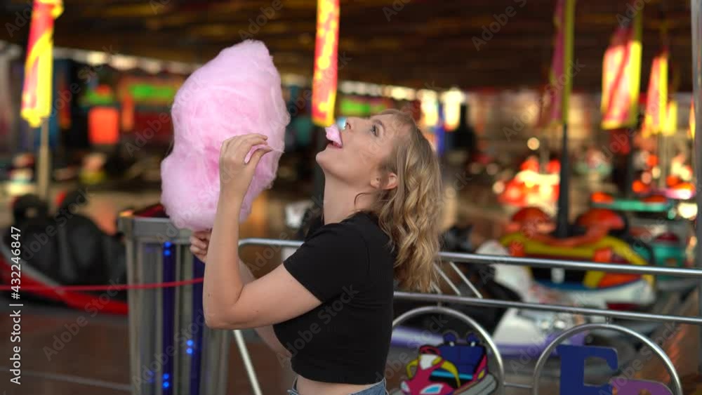Chica rubia guapa con algodón de azucar rosa sonriendo en zona de atracciones de una feria