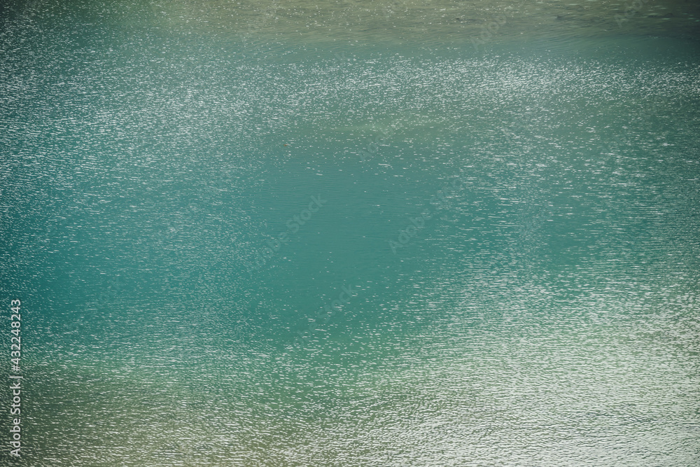 Obraz premium Texture of green blue calm water of lake. Meditative ripples on water surface. Nature minimal background of green blue lake with golden shine. Natural backdrop of lake fragment with clear azure water.