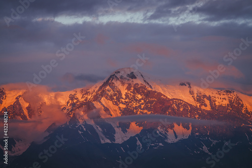 Schilderij op canvas Scenic mountain landscape with great snowy mountains lit by dawn sun among low clouds