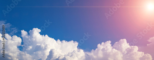 Blue sky background with white puffy clouds on a bottom foreground. Panorama with fluffy clouds and sun flares. Banner, copy space, blank space for text photo