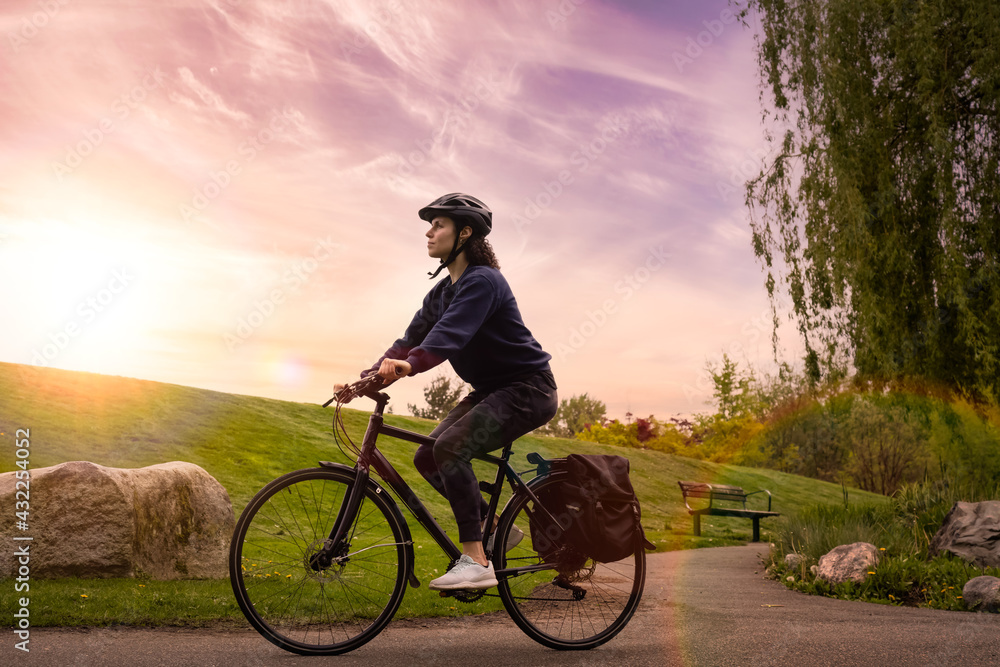 Obraz premium Adult Caucasian Woman Riding a Bicycle on a path in a modern city park. Sunset Art Render. Taken in Hawthorne Rotary Park, Surrey, Vancouver, British Columbia, Canada.