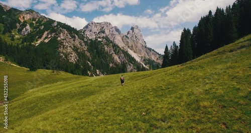 austrian alps guy hiking through grass field mountain panorama aerial overview following 4k