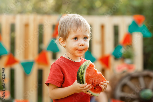 Happy child eating watermelon in the garden. Funny kid eating watermelon outdoors in summer park. Portrait of beautiful boy holding watermelon on summer day. Portrait of cute handsome in nature