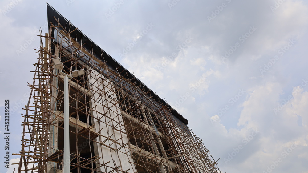 Wooden scaffolding on the side of the building under construction. Temporary wooden scaffold for workers to plaster and paint the building in bottom view on a white cloud sky background.