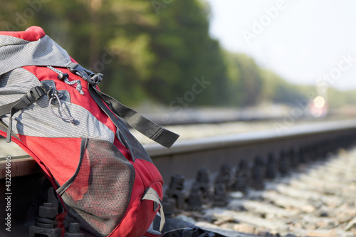 Red backpack at the railway on the background of a pine forest and the lights of the approaching train. Travel concept