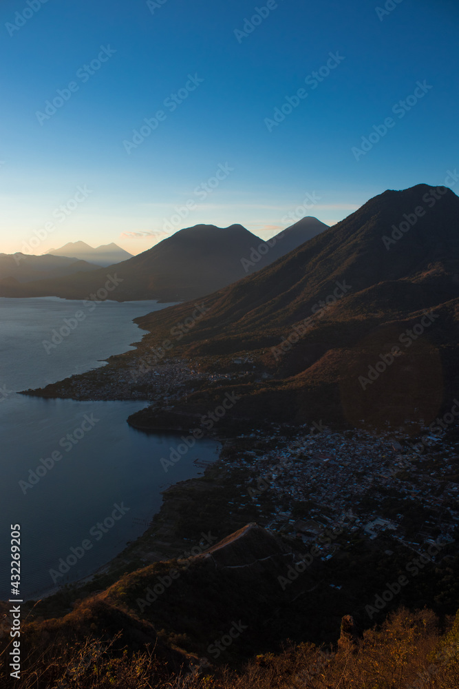Small town on the shore of the lake surrounded by mountains and volcanoes in the early hours of a warm summer morning with a beautiful cloudscape. Small town on the shore of the lake surrounded by mountains and volcanoes in the early hours of a warm summer morning with a beautiful cloudscape.