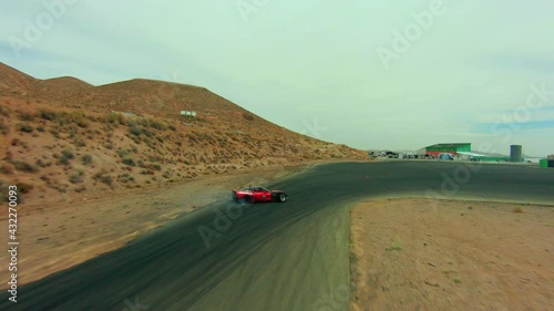 A red supercar speedster drifts around a tight turn on a racetrack while trailing smoke - aerial view