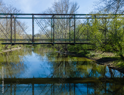 A rusty abandoned steel truss bridge over a small slow moving river. 