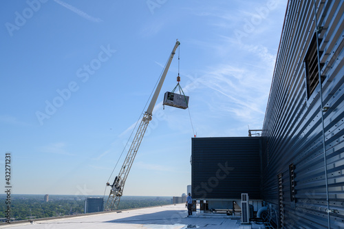 Large commercial chiller air conditioner being lifted onto roof of high rise office building.