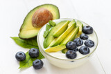 Organic yogurt topped with avocado and blueberry on white wooden background, healthy and nutritious diet