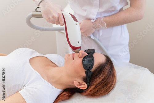 Close-up of laser hair removal on a woman's face. The doctor removes unwanted hair from the patient above the lip with an electric device
