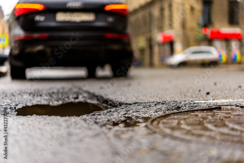 Rainy day in the big city, the car drive along the old road. Close up view of a hatch at the level of the asphalt