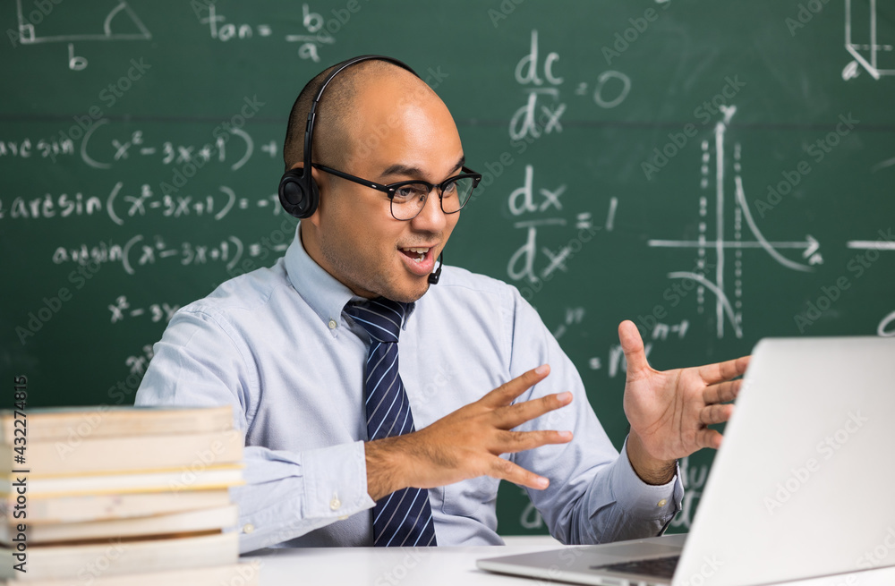 Indian young teacher man sitting wearing headset teaching online video conference live stream by laptop. Asian teacher teaching mathematics class webinar online for students learning.