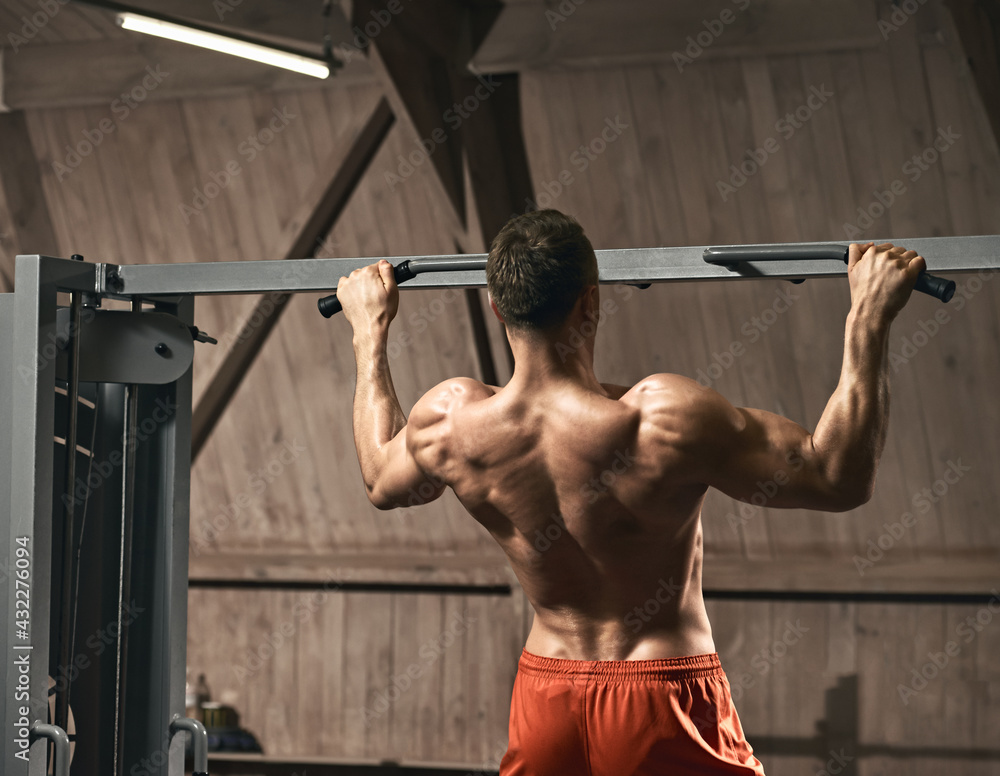 Rear view of muscular strong man training in gym and doing exercise for back Rear view of muscular strong man training in gym and doing exercise for back