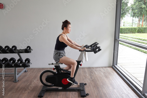 Beautiful attractive middle age southeast Asian woman exercising stationary bicycle cycle bike in a gymnasium healthy lifestyle look forward