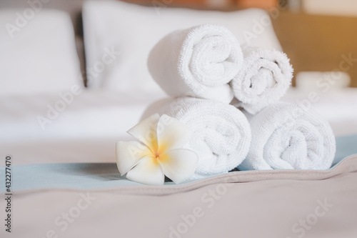 hygiene white rolled towel and blooming plumeria flower on cleaned bed in bedroom