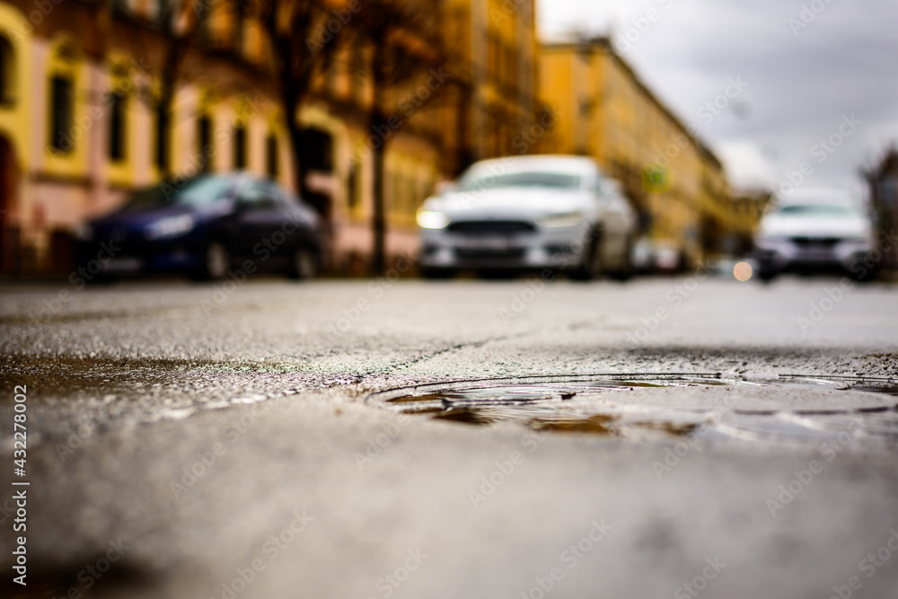Rainy day in the big city, the approaching car. Close up view of a hatch at the level of the asphalt
