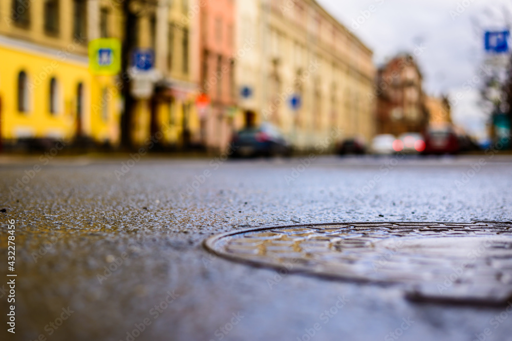 Rainy day in the big city, the parked cars on an empty road. Close up view of a hatch at the level of the asphalt